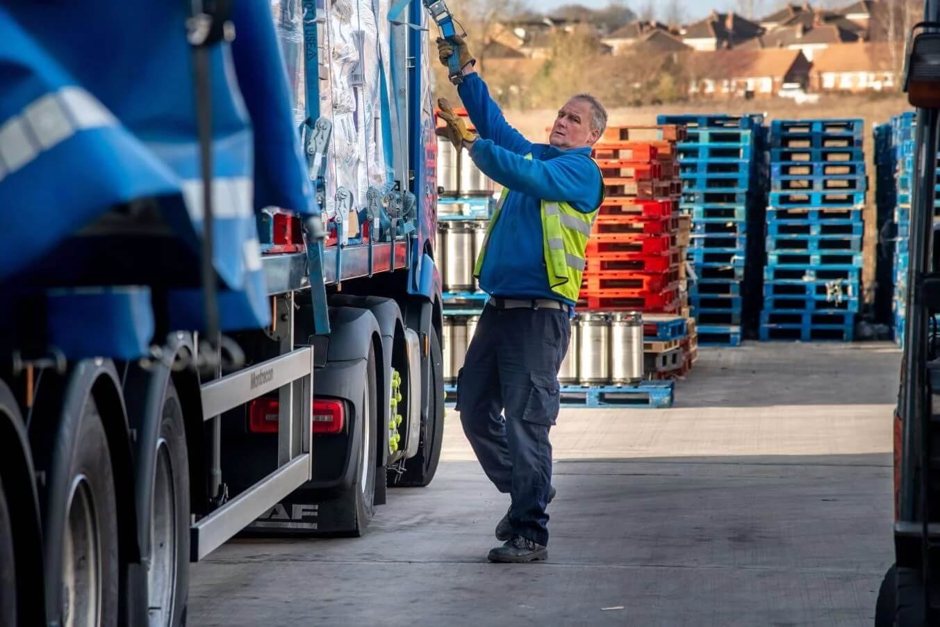 A worker in a blue jacket and high-visibility vest secures cargo on a truc